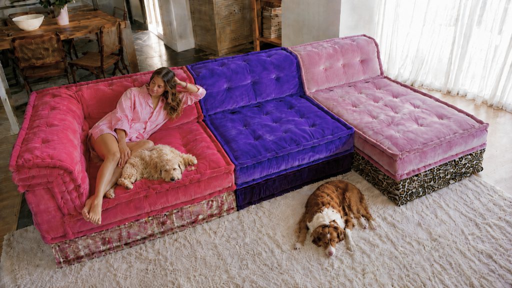 A woman relaxing on the Adorn Croft Esther Colorful Sofa in pink performance fabric with two dogs