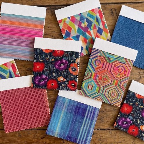 Colorful Mah Jong sofa fabric swatches including bold geometric prints, floral patterns, striped velvet, and solid fabrics in red, blue, and pink, displayed on a wooden surface