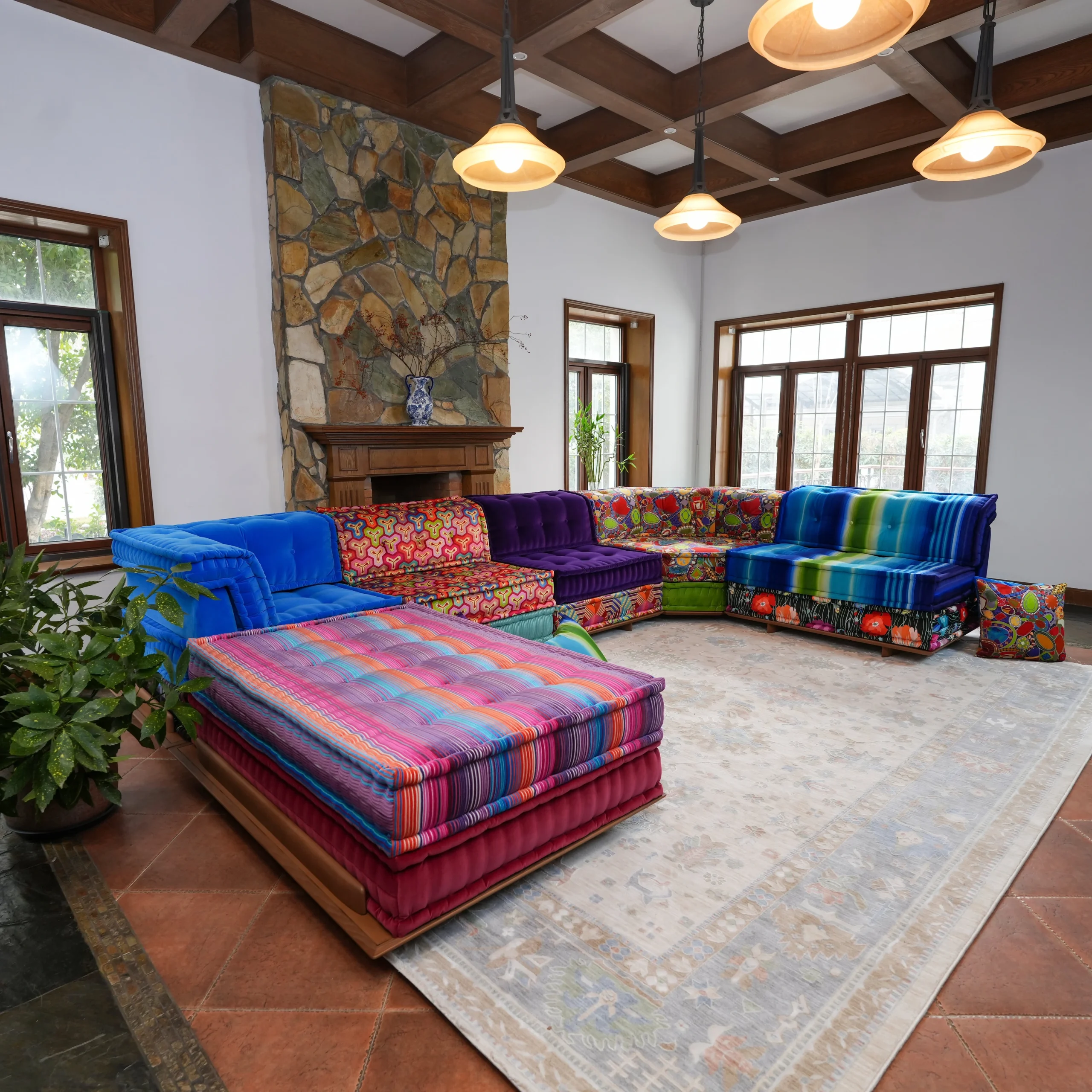 Large Mah Jong sectional sofa with wood base in colorful mixed fabrics including blue velvet, floral prints, and striped patterns, arranged in an open-plan living room