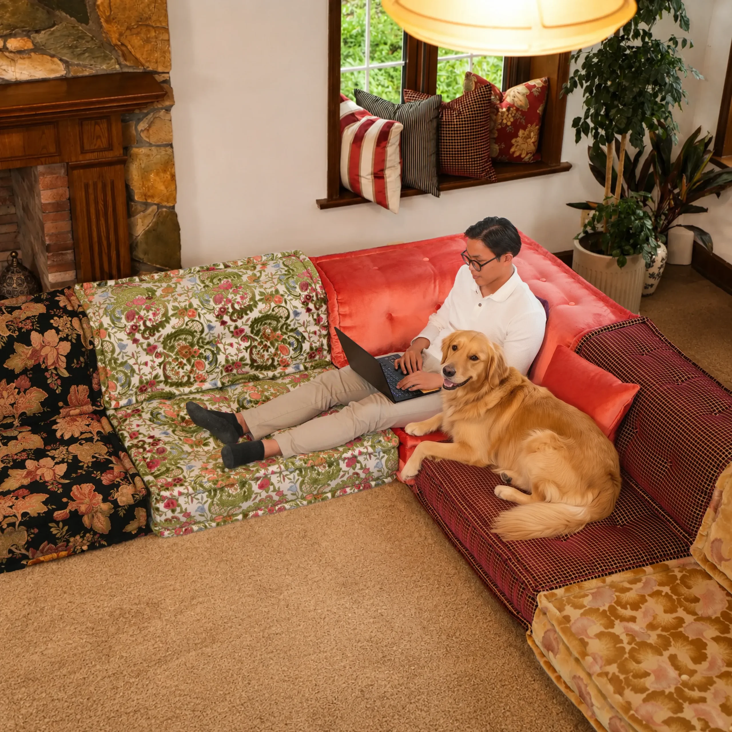 Man working on laptop with a golden retriever on a colorful Mah Jong sectional sofa in mixed floral and red velvet fabrics