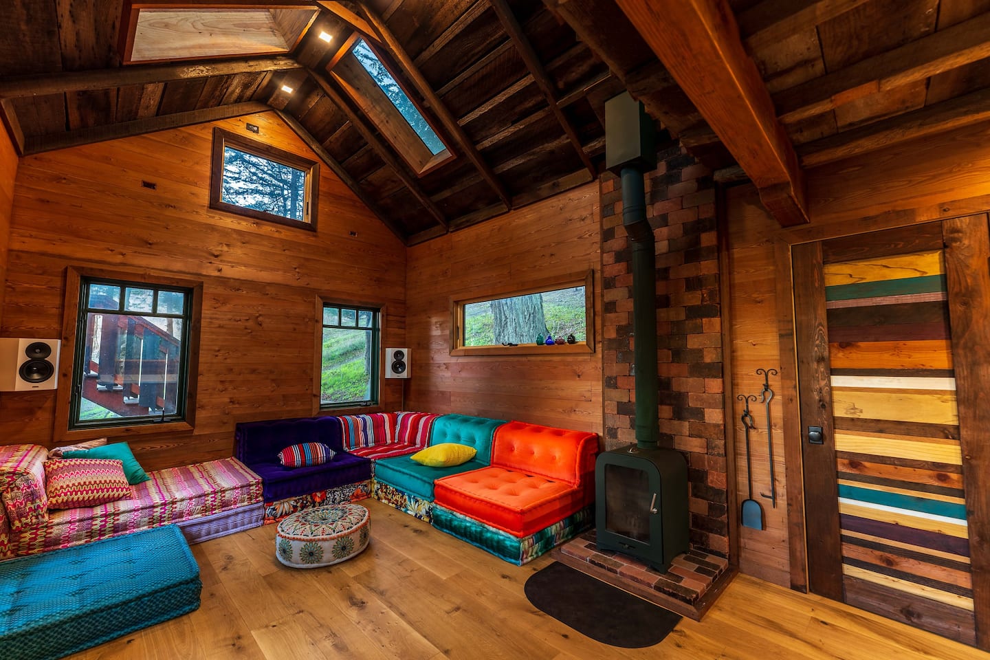 Rainbow-colored modular Mah Jong sofa in a wood-paneled treehouse living room with a wood stove
