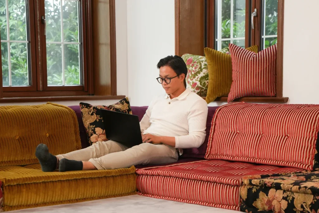 Man leaning back with a laptop on a colorful modular couch with floral cushions