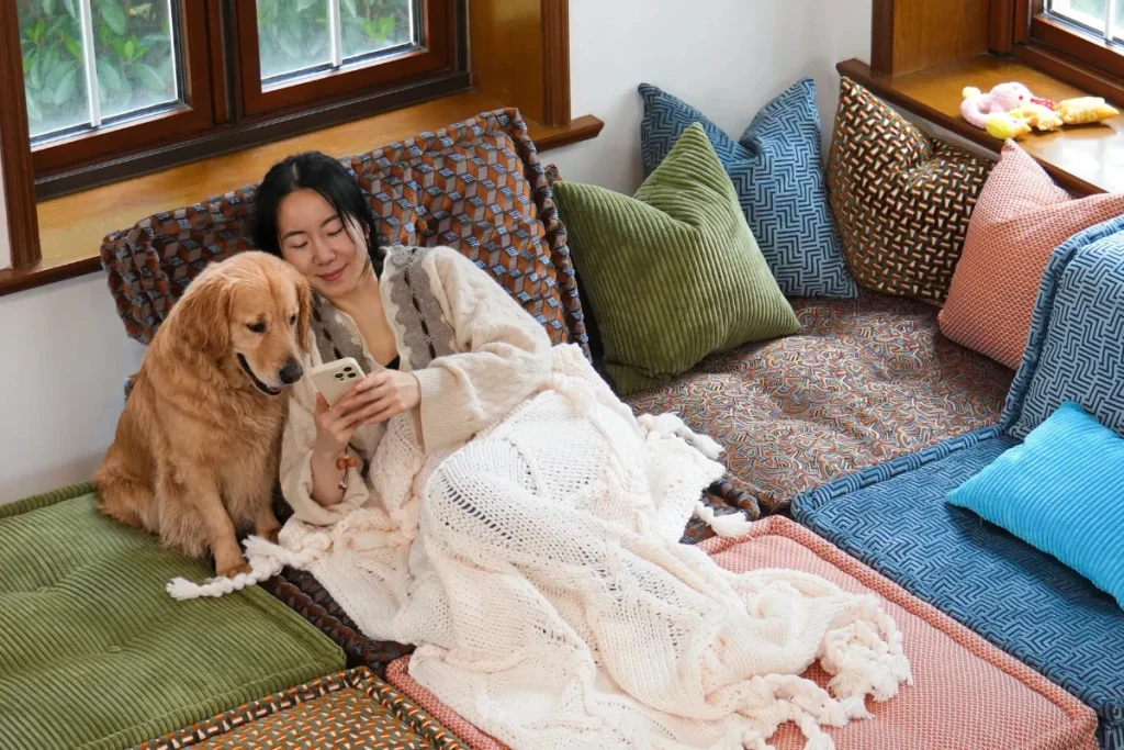 woman wrapped in a blanket relaxing with her golden retriever on a low colorful modular sofa